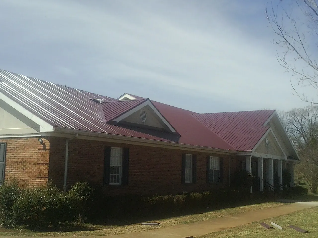 Red metal roof with gabled entries on a long brick building, from a Hail Damage Roof Repair job in Wilsonville